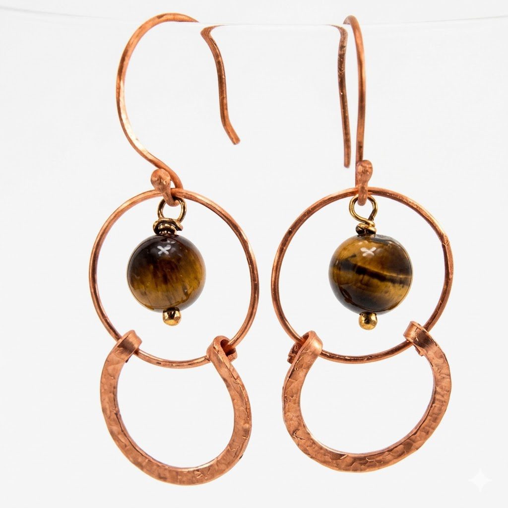 Paire de boucles d'oreilles artisanales en cuivre martelé ornées de perles rondes d'œil de tigre.