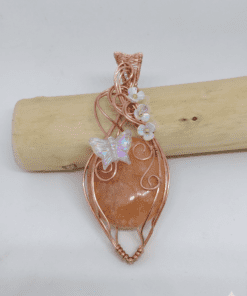 Pendentif artisanal Alara, agate orange entourée de cuivre wire wrapped, motif papillon et fleurs irisées.