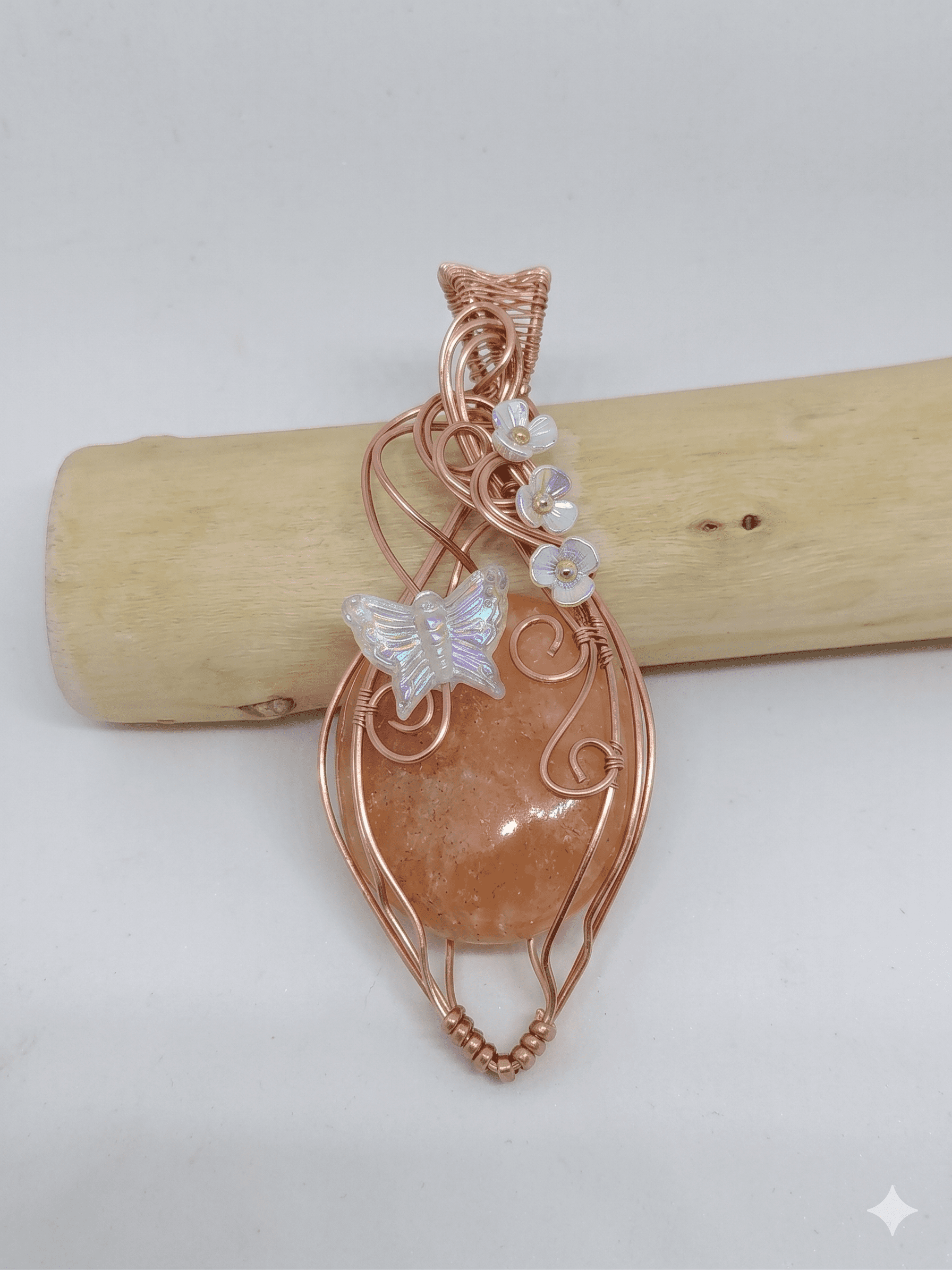 Pendentif artisanal Alara, agate orange entourée de cuivre wire wrapped, motif papillon et fleurs irisées.