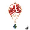 Suncatcher artisanal Finna suspendu à une branche d'arbre, composé de perles de corail rouge et d'un prisme en cristal projetant des reflets arc-en-ciel.