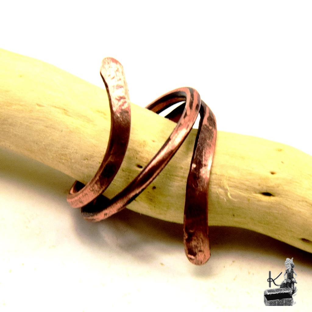 Bague artisanale Hobri en cuivre naturel brut portée sur une main dans une ambiance de forêt mystique.