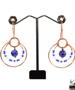 Paire de boucles d'oreilles pendantes artisanales Bega en cuivre naturel et perles de lapis-lazuli sur fond de nature.