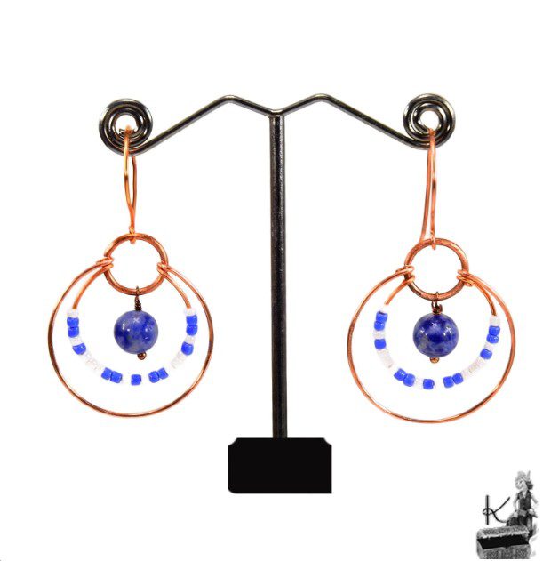 Paire de boucles d'oreilles pendantes artisanales Bega en cuivre naturel et perles de lapis-lazuli sur fond de nature.