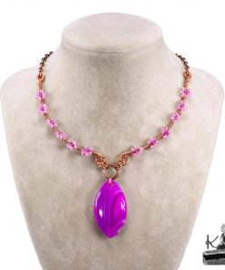 Collier bohème artisanal Galla en cuivre naturel et cabochon en agate bandée posé sur un fond inspiré de la nature.