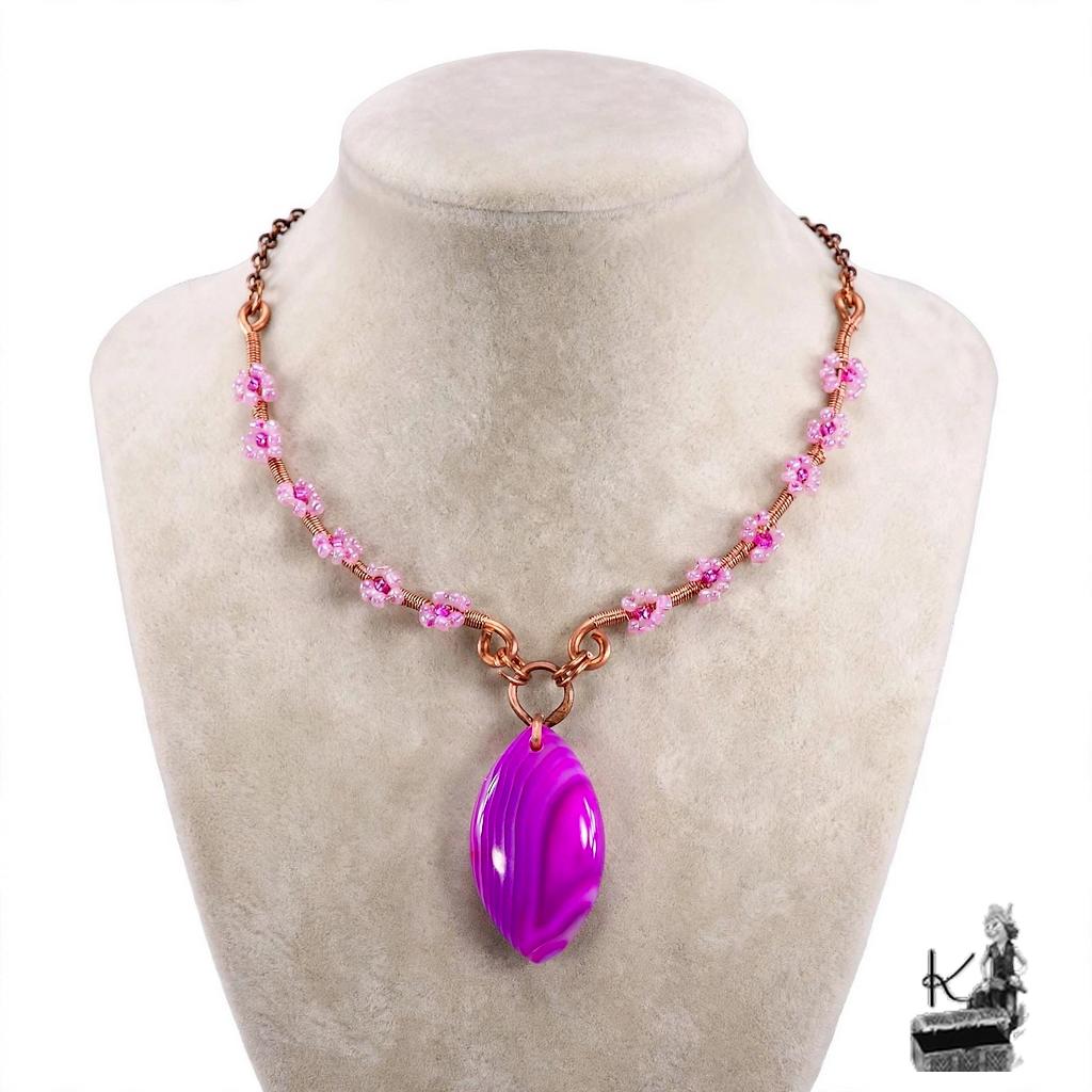 Collier bohème artisanal Galla en cuivre naturel et cabochon en agate bandée posé sur un fond inspiré de la nature.