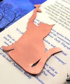 Marque-page chat en cuivre découpé à la main, posé sur un livre ancien près d'une bougie, accessoire de lecture féérique.