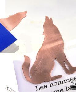Marque-page loup en cuivre découpé à la main, posé sur un grimoire ouvert près d'une bougie, accessoire de lecture féérique.