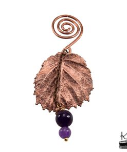 Poids pour sachet de thé Céleste en cuivre avec feuille de bouleau et perles d'améthyste, posé sur une tasse pour un rituel de bien-être.