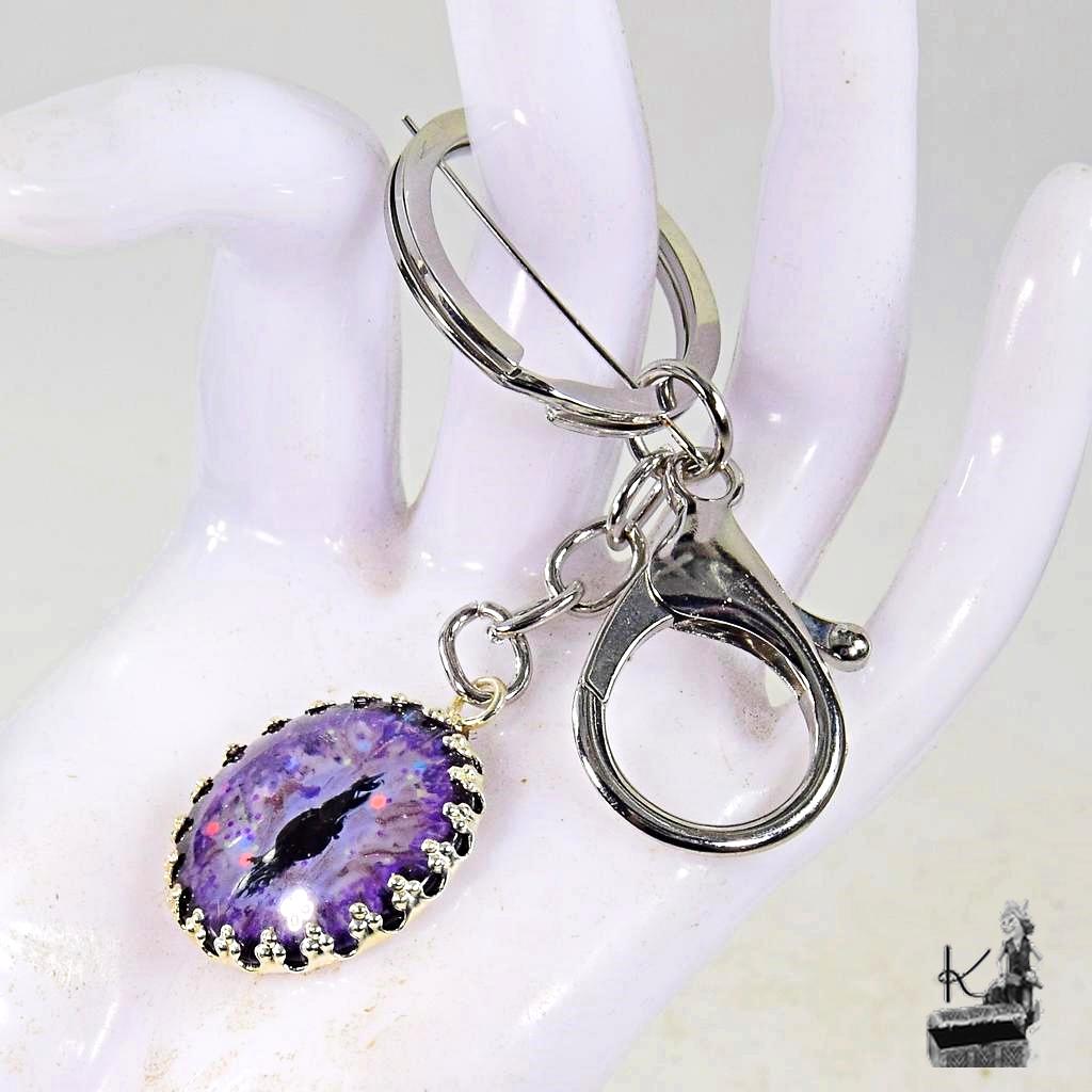 Porte-clé artisanal en métal argenté avec un œil de dragon peint à la main, création magique de la boutique Le Trésor des Korriganes.