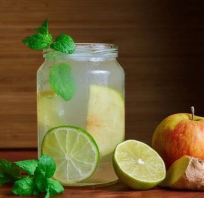 Carafe remplie de switchel frais, une boisson désaltérante naturelle à base de vinaigre de cidre, sirop d'érable et gingembre, servie avec des glaçons.
