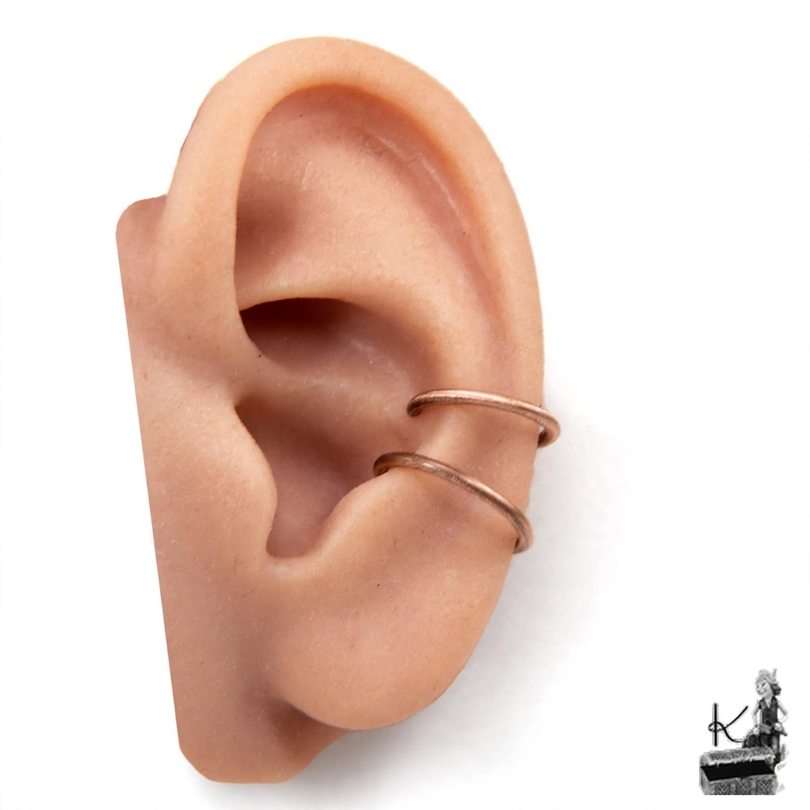 Gros plan sur un ear cuff double onde minimaliste sans perçage en cuivre pur patiné, porté sur le cartilage de l'oreille.